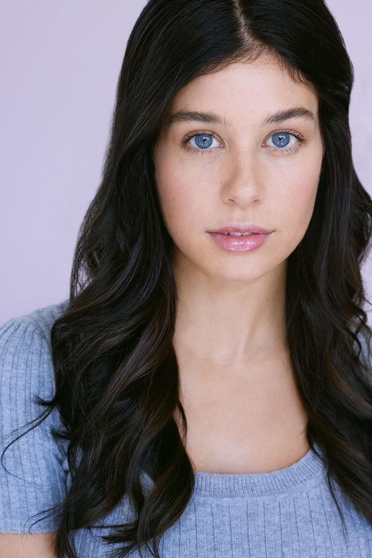 Actor Carly Tway in front of light pink background to bring out her blue eyes.